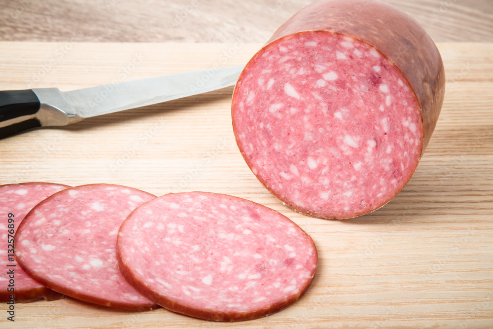 Smoke-dried sausage with slices and knife on the wooden board in the kitchen. Smoke-dried sausage with slices and knife on the wooden board in the kitchen.
