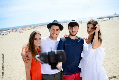group of four young people making selfie on the beach during summer