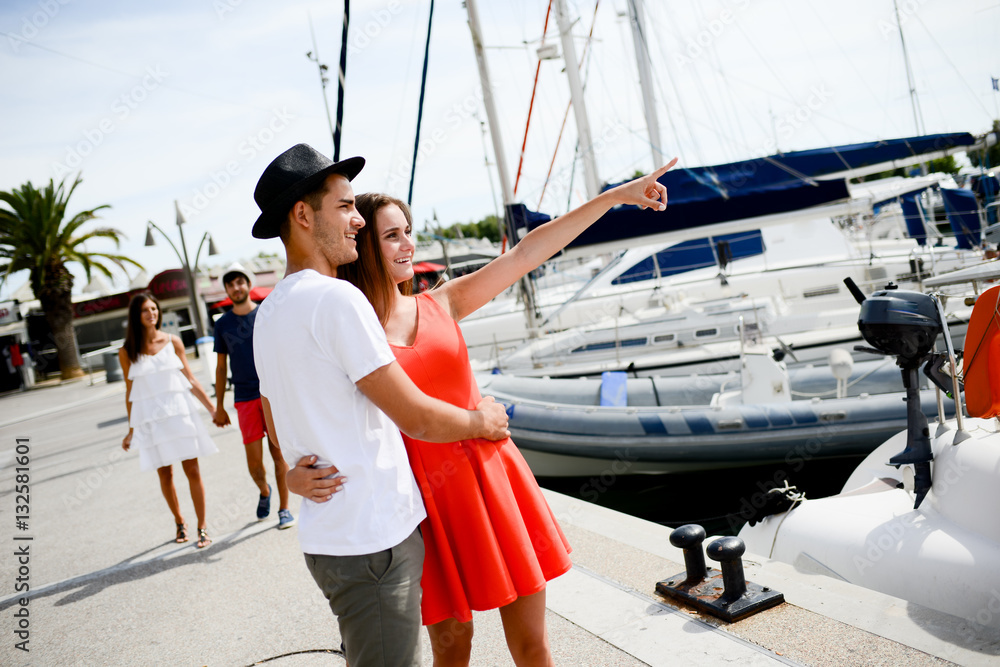 happy young couple walking by the harbor of a touristic sea resort with sailboats on background happy young couple walking by the harbor of a touristic sea resort with sailboats on background
