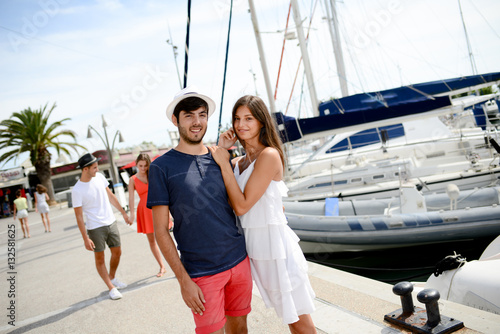 happy young couple walking by the harbor of a touristic sea resort with sailboats on background © W PRODUCTION