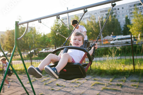 Happy baby boy having fun on a swing on summer day