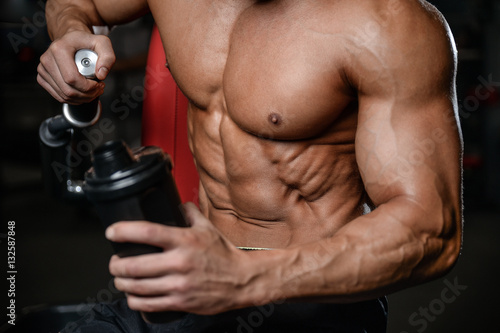 Handsome fitness model holding a shaker in the gym gain muscle.