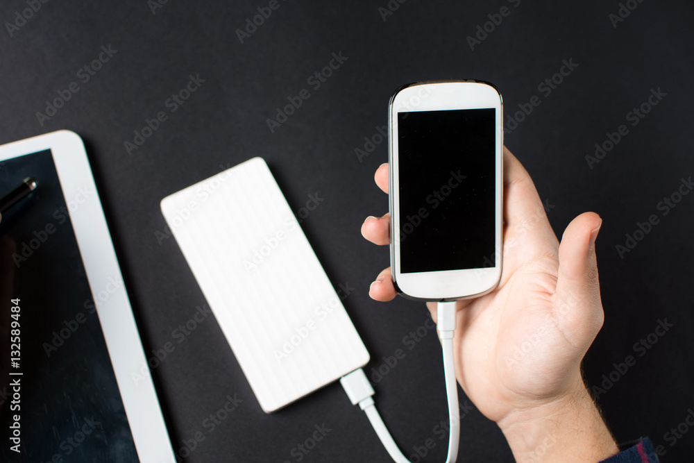 male hands holding a white cellphone connected to a power bank male hands holding a white cellphone connected to a power bank