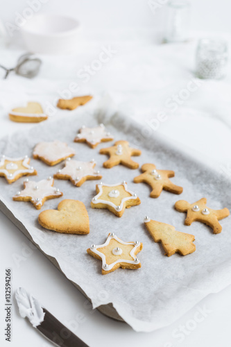 Decorating Christmas Shortbread Biscuits on Baking Tray with Vanilla Icing and Silver Sugar Balls on White Table