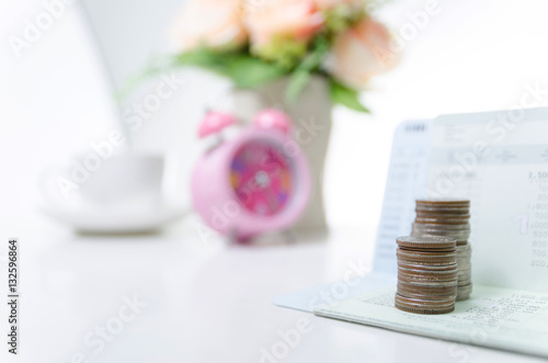 Stack of coins on saving bank accound book and alarm clock on th photo