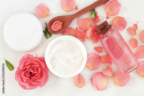 Skincare beauty treatment plant-based products with wink rose petals. Jar of body moisturizer, attar bottle toning lotion, top view homemade cosmetic ingredients. 