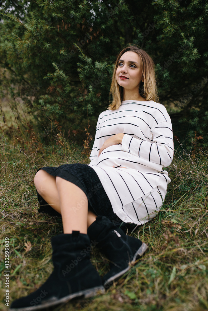 pregnant woman is sitting on grass and holding her hands on her swollen belly. pregnancy, motherhood, people and expectation concept pregnant woman is sitting on grass and holding her hands on her swollen belly. pregnancy, motherhood, people and expectation concept
