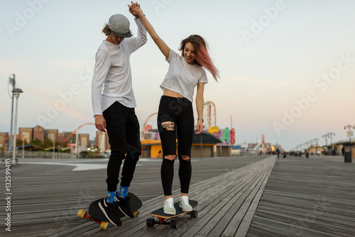 Young couple learning how to ride a longboard, holding hands photo