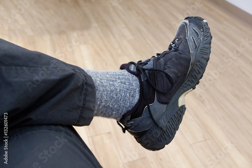 Person seated and waiting. Close-up of crossed legs, shoe, sock and pants. Horizontal.