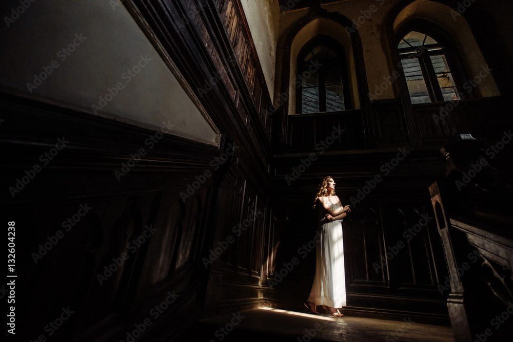 Indoor summer portrait of young pretty cute girl. Beautiful woman posing beside fairytale window inside cabinet, scars old castle. Bride standing in white atlas dress on desk stairs. Photo has model. Indoor summer portrait of young pretty cute girl. Beautiful woman posing beside fairytale window inside cabinet, scars old castle. Bride standing in white atlas dress on desk stairs. Photo has model.