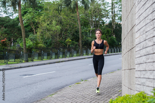 Sport fitness model jogging on sidewalk in quiet city district. Female athlete training outdoors.