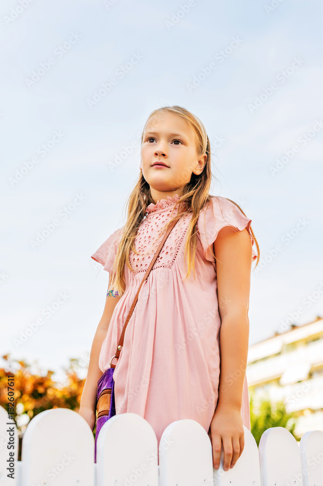 Outdoor portrait of cute 8-9 year old girl wearing pink dress