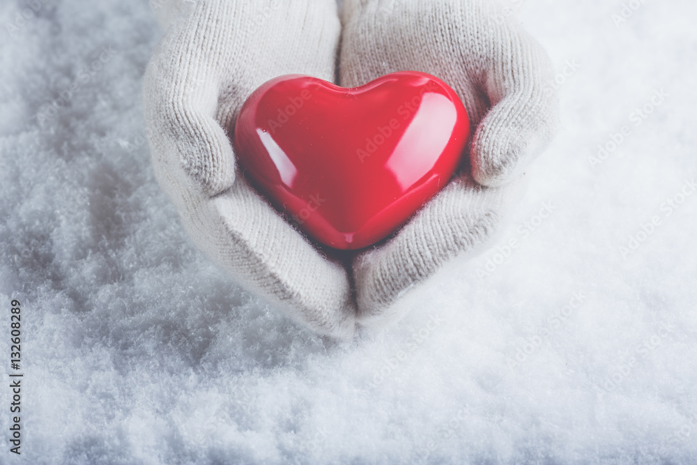 Female hands in white knitted mittens with a glossy red heart on