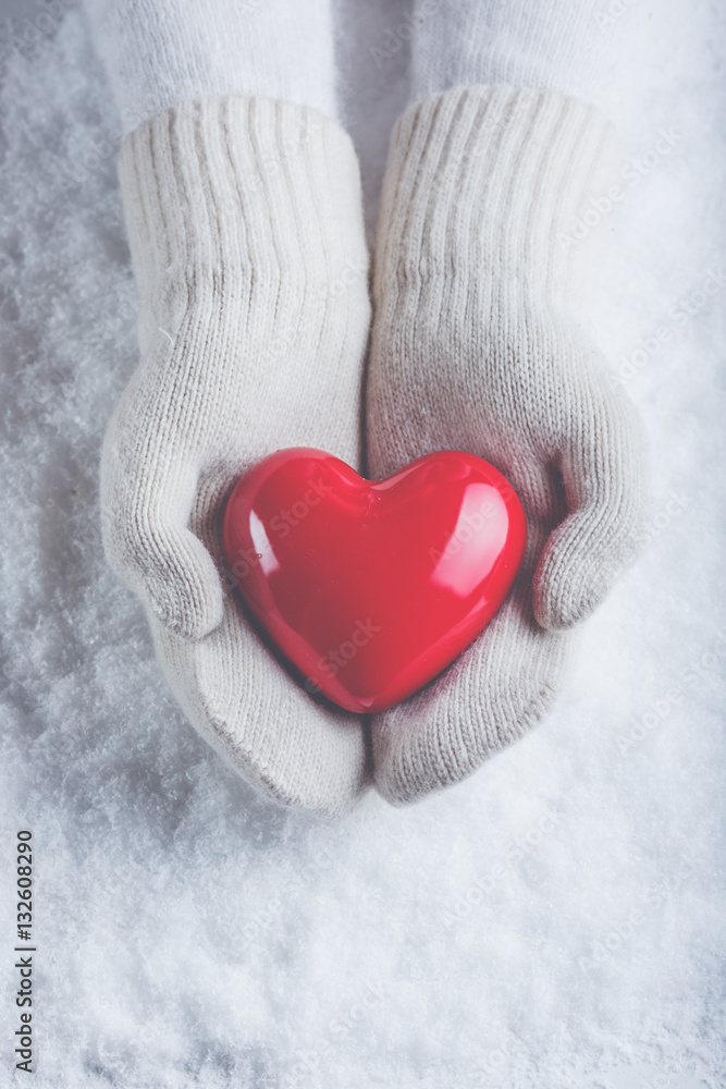 Female hands in white knitted mittens with a glossy red heart on