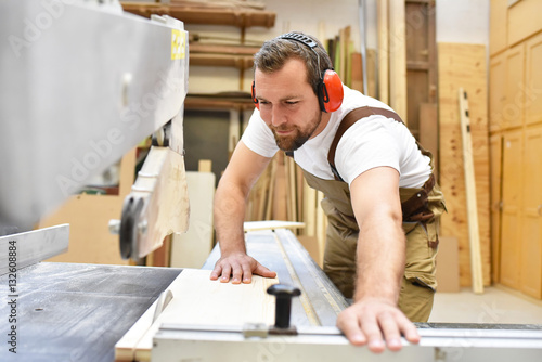 Tischler sägt Holzbrett in einer Schreinerei // Carpenter sawing wooden board in a carpenter's workshop photo