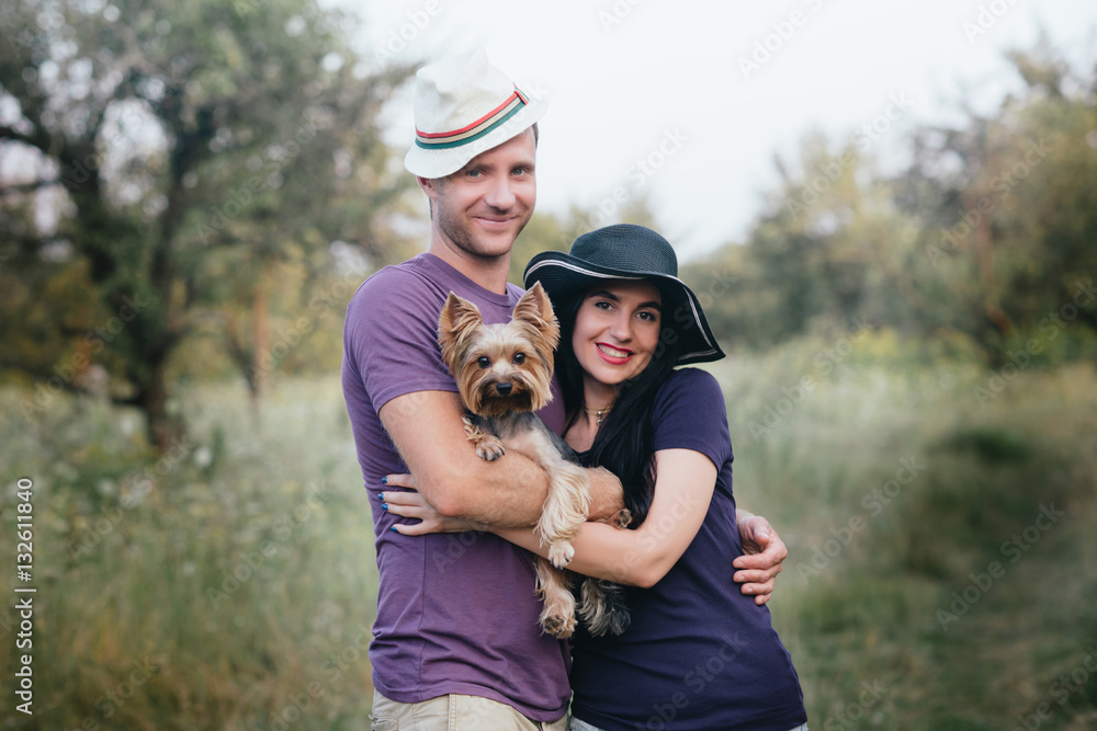 Young couple with little dog yorkshire terrier dressed  t-shirt and hat embracing and have fun on the road,travel, vacation, holidays, vacation, love, life style