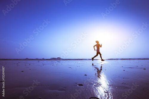 running, silhouette of runner on the beach at sunset, blue background with copyspace and reflection