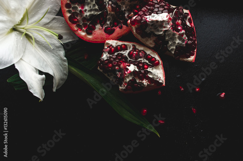 Delicious pomegranate fruit and lilies on black background. Stil