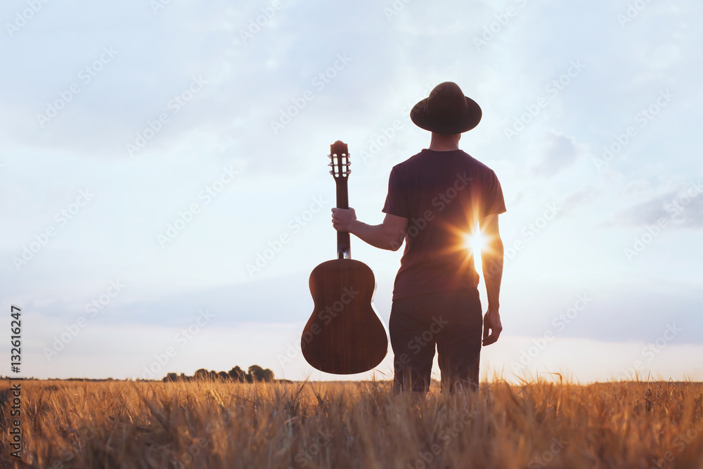 Fototapeta premium music festival background, silhouette of musician artist with acoustic guitar at sunset field.