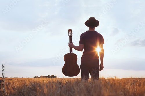 Photo music festival background, silhouette of musician artist with acoustic guitar at sunset field