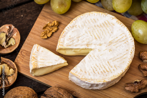 Camembert cheese with walnuts and green grapes on wooden rustic background