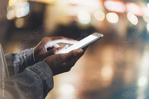 Girl pointing finger on screen smartphone on background illumination bokeh color light in night atmospheric city, hipster using hands and texting mobile phone, mockup glitter street, content lifestyle