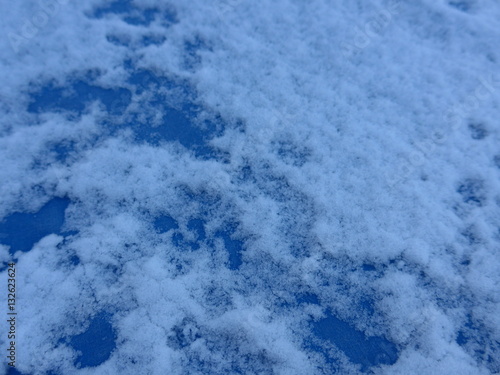 Schnee und Eis auf einem gefrorenen Fensterglas vor blauem Himmel