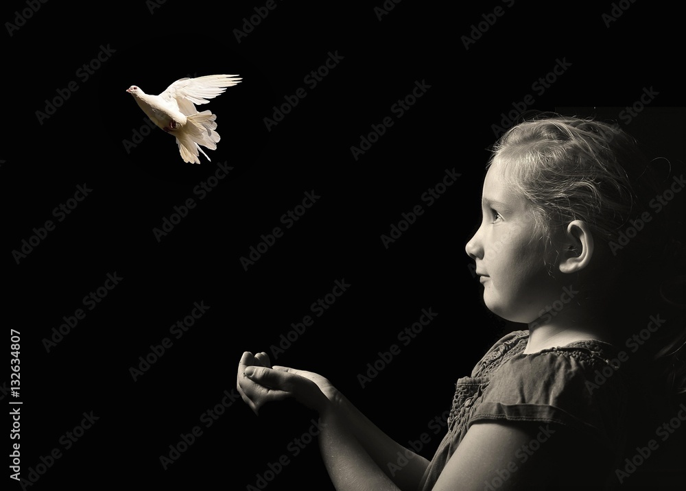 The little girl releasing a white dove from hands . Symbol of peace on a black background.