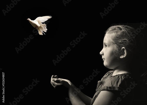 Obraz na płótnie The little girl releasing a white dove from hands . Symbol of peace on a black background. w salonie