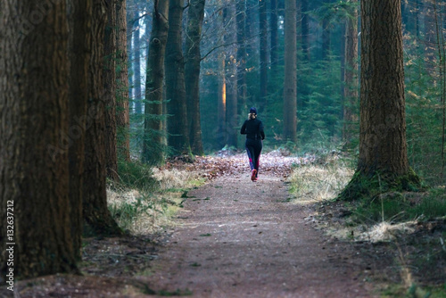 Woman running on path in winter pine forest. Rear view. © ysbrandcosijn