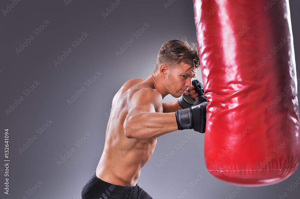 Muscular Fighter Practicing Some Kicks with Punching Bag. Boxing on the Gray Background. Concept of Healthy Lifestyle.