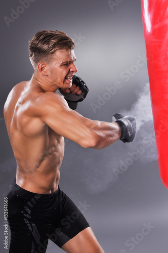 Muscular Fighter Practicing Some Kicks with Punching Bag. Boxing on the Gray Background. Concept of Healthy Lifestyle. © cirkoglu