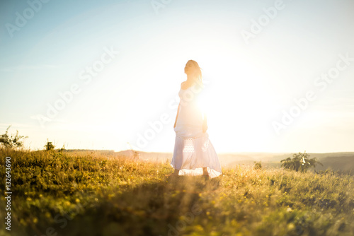 Young romantic woman on the meadow at sunset. The girl in the white dress enjoys the outdoors. Warm light . Strong glow of the sun behind the girl