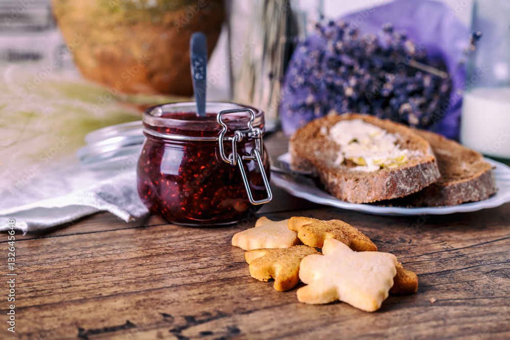 Homemade sugar honey cookies, raspberry jam in jar, bread and butter, knife, on a wooden background. Breakfast concept.