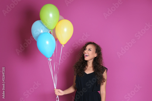 Beautiful African American woman in party cap with air balloons on color background