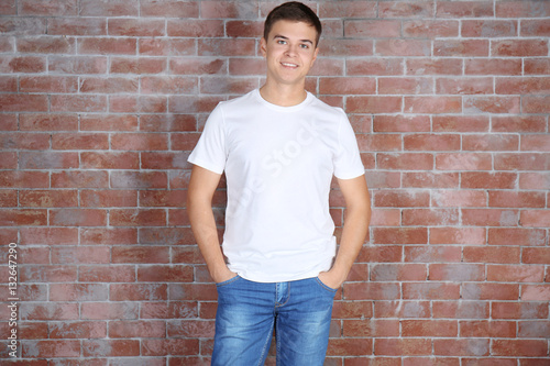 Handsome young man in blank white t-shirt standing against brick wall
