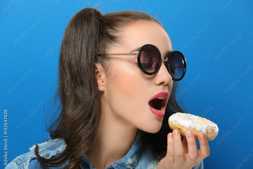 Funny young woman eating tasty donut on blue background Funny young woman eating tasty donut on blue background
