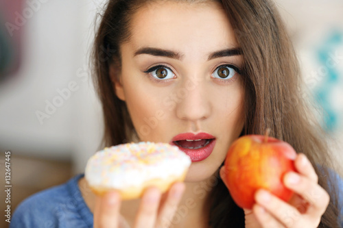 Beautiful young woman making choice between apple and donut  close up