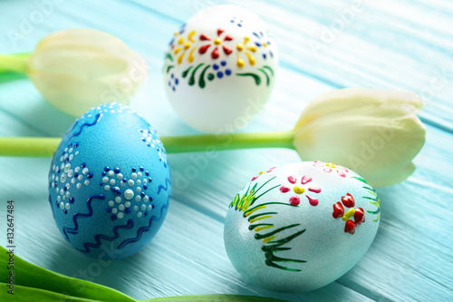 Beautiful Easter composition with decorated eggs and flowers on blue wooden background, closeup
