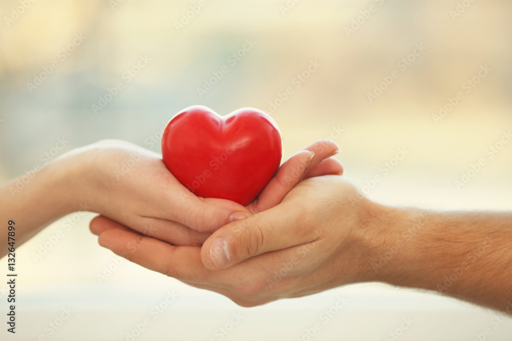 Male and female hands holding small red heart on blurred background