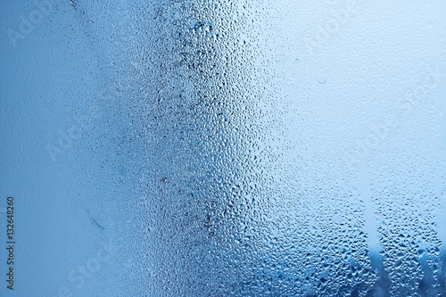 Window glass with condensation, strong, high humidity in the room, large water droplets flow down the window, cold tone, natural water drops on window glass