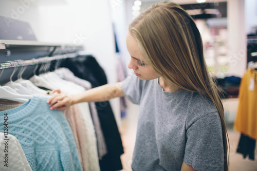 Beautiful blonde buys new things in a clothing store. Seller works in  boutique