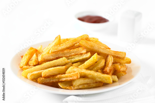 Fresh homemade crispy French fries on plate with a small bowl of ketchup and salt shaker in the back, photographed with natural light (Selective Focus, Focus in the middle of the image)