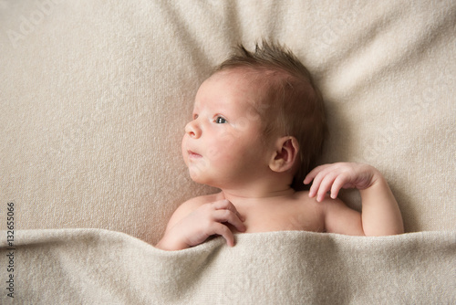Newborn baby lies on a grey blanket and looking to the side