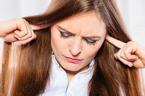 Stressed woman with closed eyes put fingers in ears,