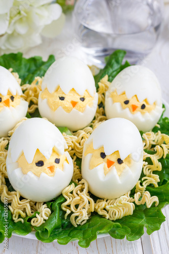 Little chicken in nest, deviled eggs served with salad and dry ramen on white plate, vertical