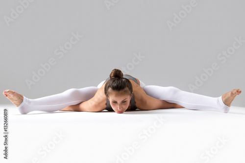 Young attractive woman practicing yoga  sitting in Tortoise  Turtle exercise  Kurmasana pose  working out wearing sportswear  indoor full length  isolated against grey studio background