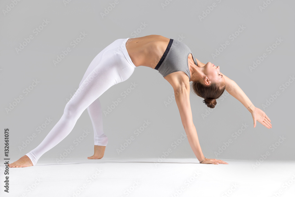 Young attractive woman practicing yoga, stretching in Wild Thing,  Flip-the-Dog exercise, Camatkarasana pose, working out wearing sportswear,  indoor full length, isolated against grey studio background Stock Photo