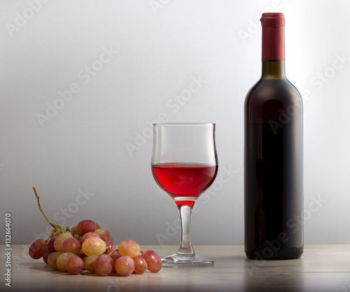 Красное вино в бокале,гроздь винограда и бутылка вина на столе.