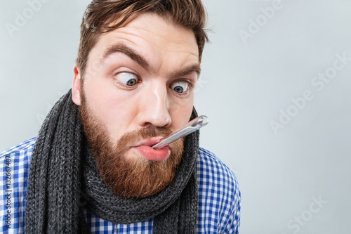 Obraz na płótnie Funny bearded man in scarf with thermometer at his mouth